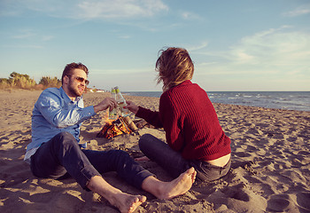 Image showing Young Couple Sitting On The Beach beside Campfire drinking beer