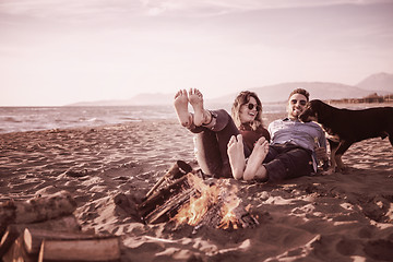 Image showing Young Couple Sitting On The Beach beside Campfire drinking beer