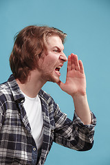 Image showing Isolated on blue young casual man shouting at studio