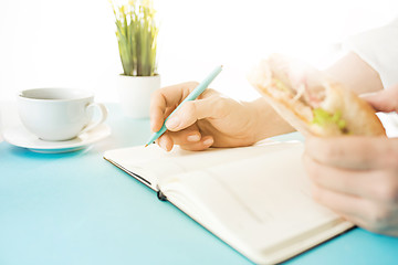 Image showing The male hands holding pen and sandwich. The trendy blue desk.