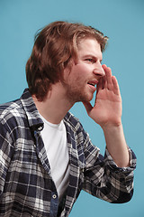 Image showing Isolated on blue young casual man shouting at studio