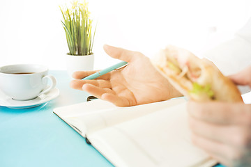 Image showing The male hands holding pen and sandwich. The trendy blue desk.