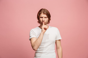 Image showing The young man whispering a secret behind her hand over pink background