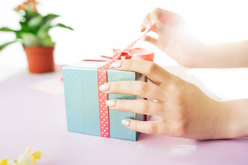 Image showing Close-up of female hands holding a present. The trendy pink desk.