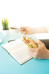 Image showing The male hands holding pen and sandwich. The trendy blue desk.