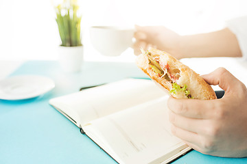 Image showing The male hands holding pen and sandwich. The trendy blue desk.