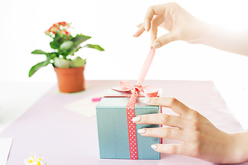 Image showing Close-up of female hands holding a present. The trendy pink desk.