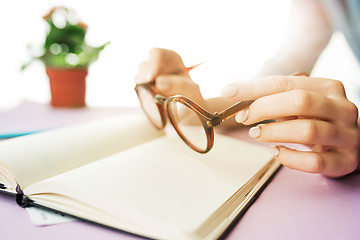 Image showing The female hands holding glasses. The trendy pink desk.