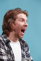 Image showing The young emotional angry man screaming on blue studio background