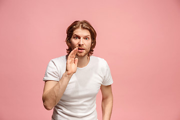 Image showing The young man whispering a secret behind her hand over pink background