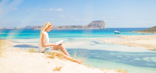 Image showing Woman reading book, enjoying sun on beach.