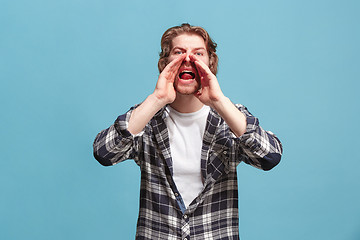 Image showing Isolated on blue young casual man shouting at studio