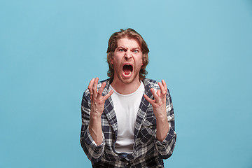 Image showing The young emotional angry man screaming on blue studio background