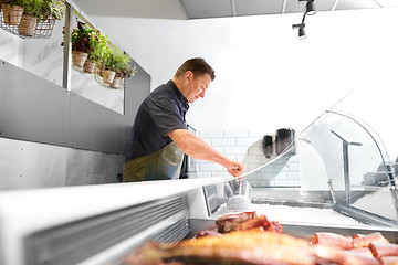 Image showing male seller adding ice to fridge at fish shop