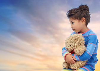 Image showing sad little girl with teddy bear over evening sky