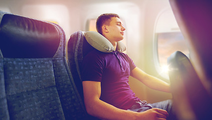 Image showing young man sleeping in plane with travel pillow