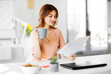 Image showing businesswoman with papers drinks coffee at office