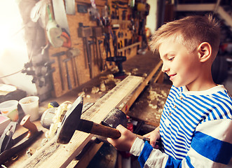 Image showing happy little boy with hammer and plank at workshop