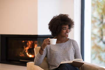 Image showing black woman reading book  in front of fireplace