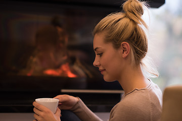 Image showing young woman drinking coffee in front of fireplace