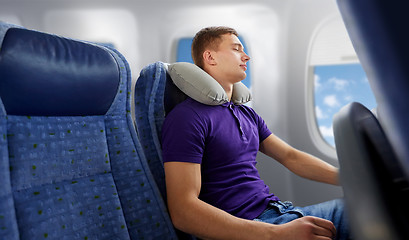 Image showing young man sleeping in plane with travel pillow