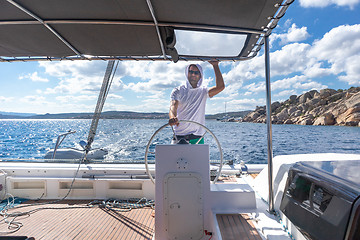 Image showing Attractive male skipper navigating the fancy catamaran sailboat on sunny summer day on calm blue sea water.