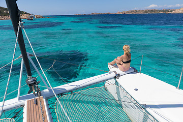 Image showing Woman relaxing on a summer sailing cruise, sitting on a luxury catamaran in picture perfect turquoise blue lagoon near Spargi island in Maddalena Archipelago, Sardinia, Italy.