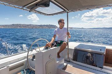 Image showing Attractive male skipper navigating the fancy catamaran sailboat on sunny summer day on calm blue sea water.