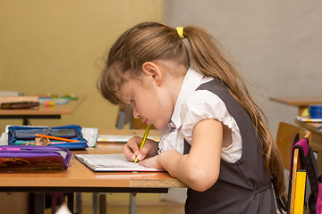 Image showing A schoolgirl in a lesson crouched writes in a notebook