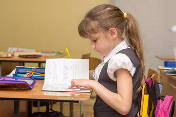 Image showing A little girl in a class carefully reads a diary entry