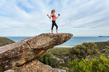 Image showing Woman listening to music or a playlist high up on a balancing rock on mountain edge.