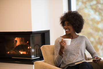 Image showing black woman reading book  in front of fireplace