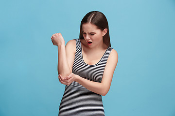 Image showing The elbow ache. The sad woman with elbow ache or pain on a blue studio background.