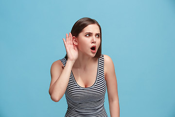 Image showing The young woman is listening something on the blue background.