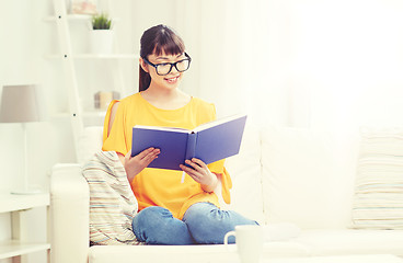 Image showing smiling young asian woman reading book at home