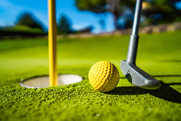 Image showing Mini Golf yellow ball with a bat near the hole at sunset