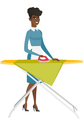 Image showing African maid ironing clothes on ironing board.