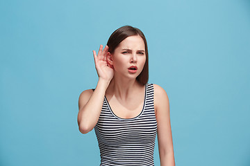 Image showing The young woman is listening something on the blue background.