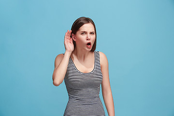 Image showing The young woman is listening something on the blue background.