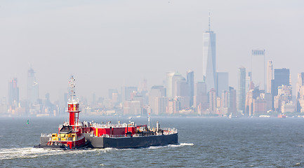 Image showing Freight tug pushing cargo ship to the port in New York City and Lower Manhattan skyscarpers skyline in background.