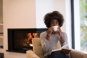 Image showing black woman reading book  in front of fireplace