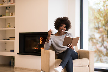 Image showing black woman reading book  in front of fireplace