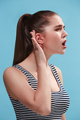 Image showing The young woman is listening something on the blue background.