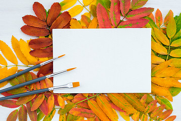 Image showing Paintbrushes and white canvas on autumn leaves background