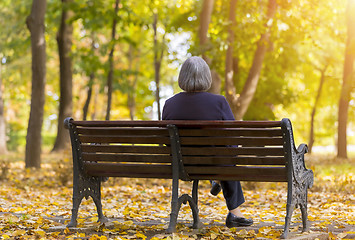 Image showing Elderly woman sitting on a bench in autumn park