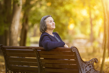 Image showing Elderly woman sitting on a bench in autumn park