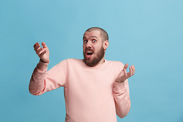 Image showing Beautiful male half-length portrait isolated on blue studio backgroud. The young emotional surprised man