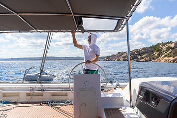 Image showing Attractive male skipper navigating the fancy catamaran sailboat on sunny summer day on calm blue sea water.