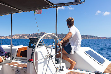 Image showing Male skipper navigating the fancy catamaran sailboat on sunny summer day on calm blue sea water.