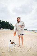 Image showing Young woman in jacket playing with dog on beach